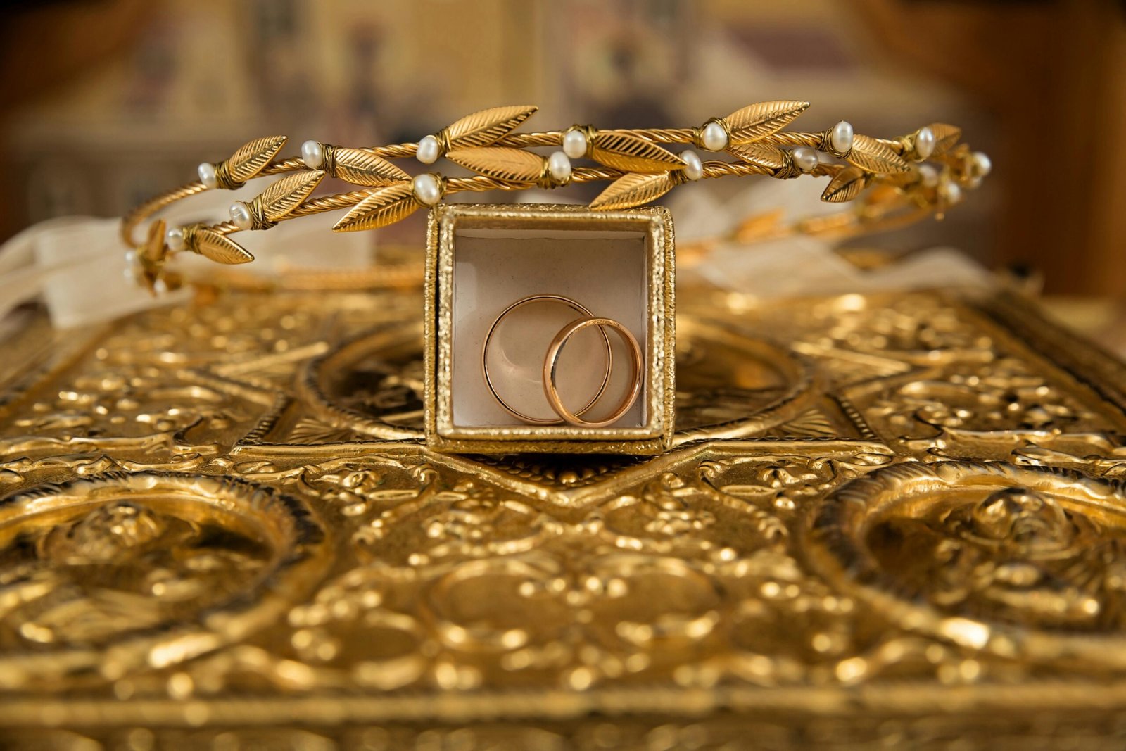 Close-up of gold wedding rings and a delicate tiara on an ornate golden background, symbolizing luxury and elegance.